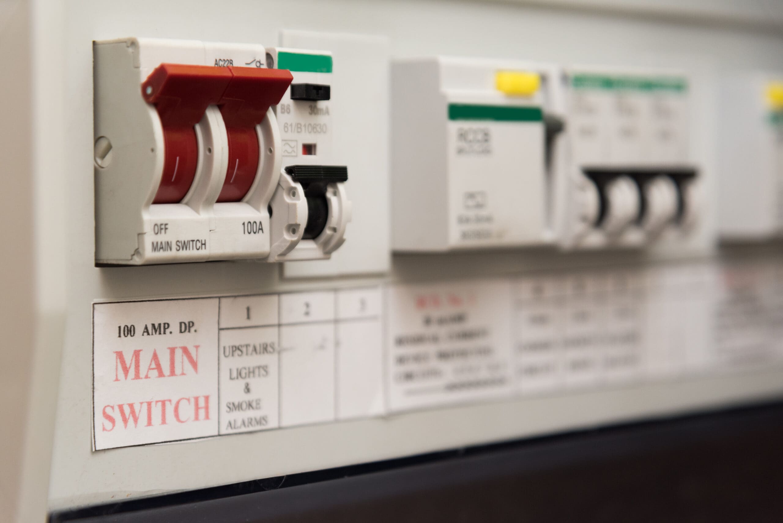 Close-up of an electrical fuse box featuring a red 100 AMP DP MAIN SWITCH, several circuit breakers, and labels—an essential component in safe Electrical Installations and rewires.