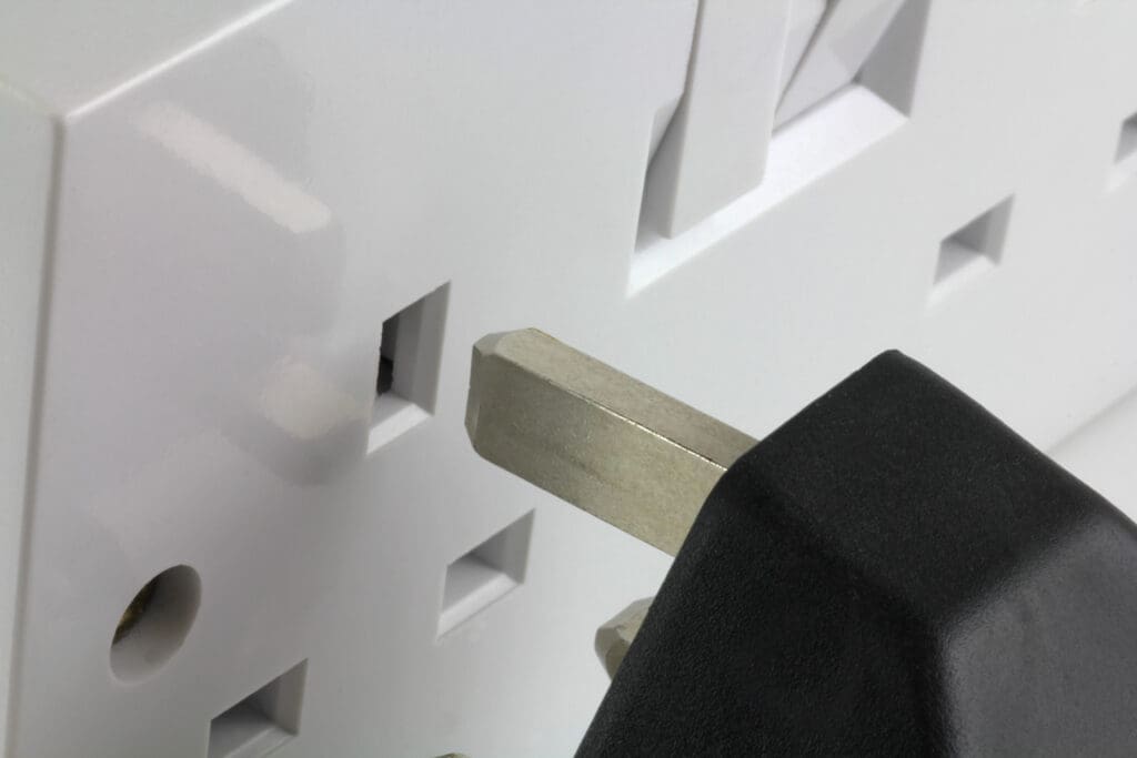 Close-up of a black three-prong electrical plug about to be inserted into a white electrical socket, highlighting the importance of proper electrical installations and safety—a key focus for any qualified electrician.